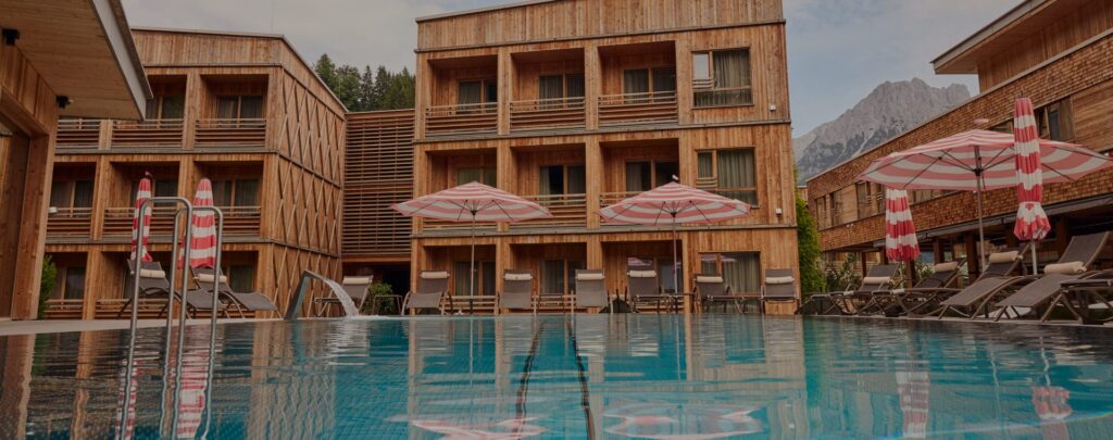 Außenansicht der Tirol Lodge Ellmau mit Pool und Sonnenschirmen